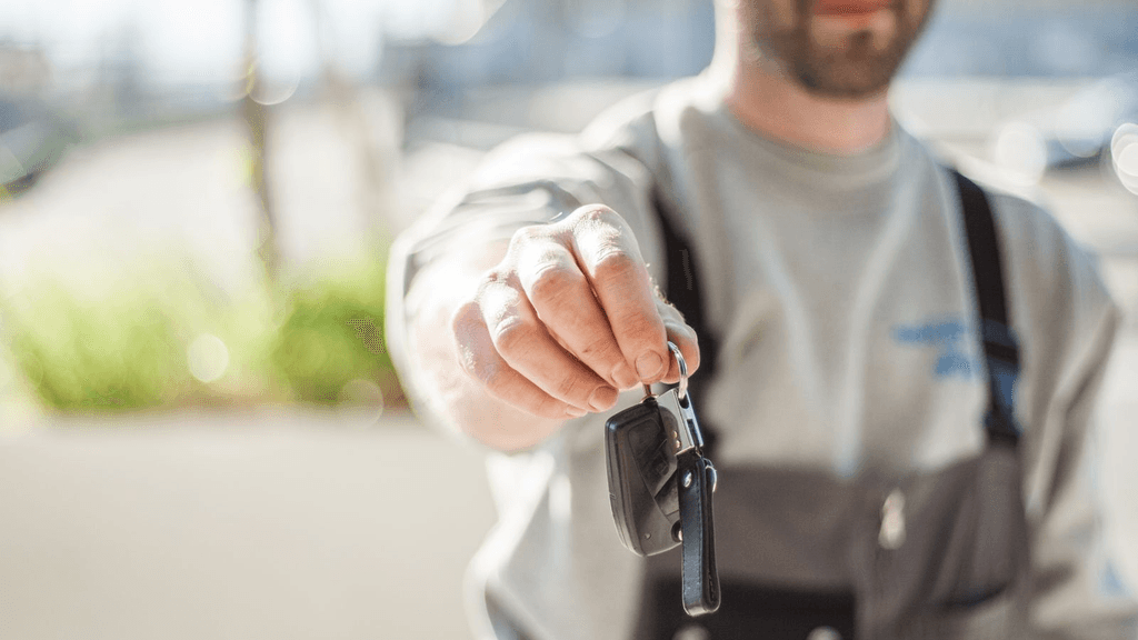 Real automotive technician holding a vehicle key near a car